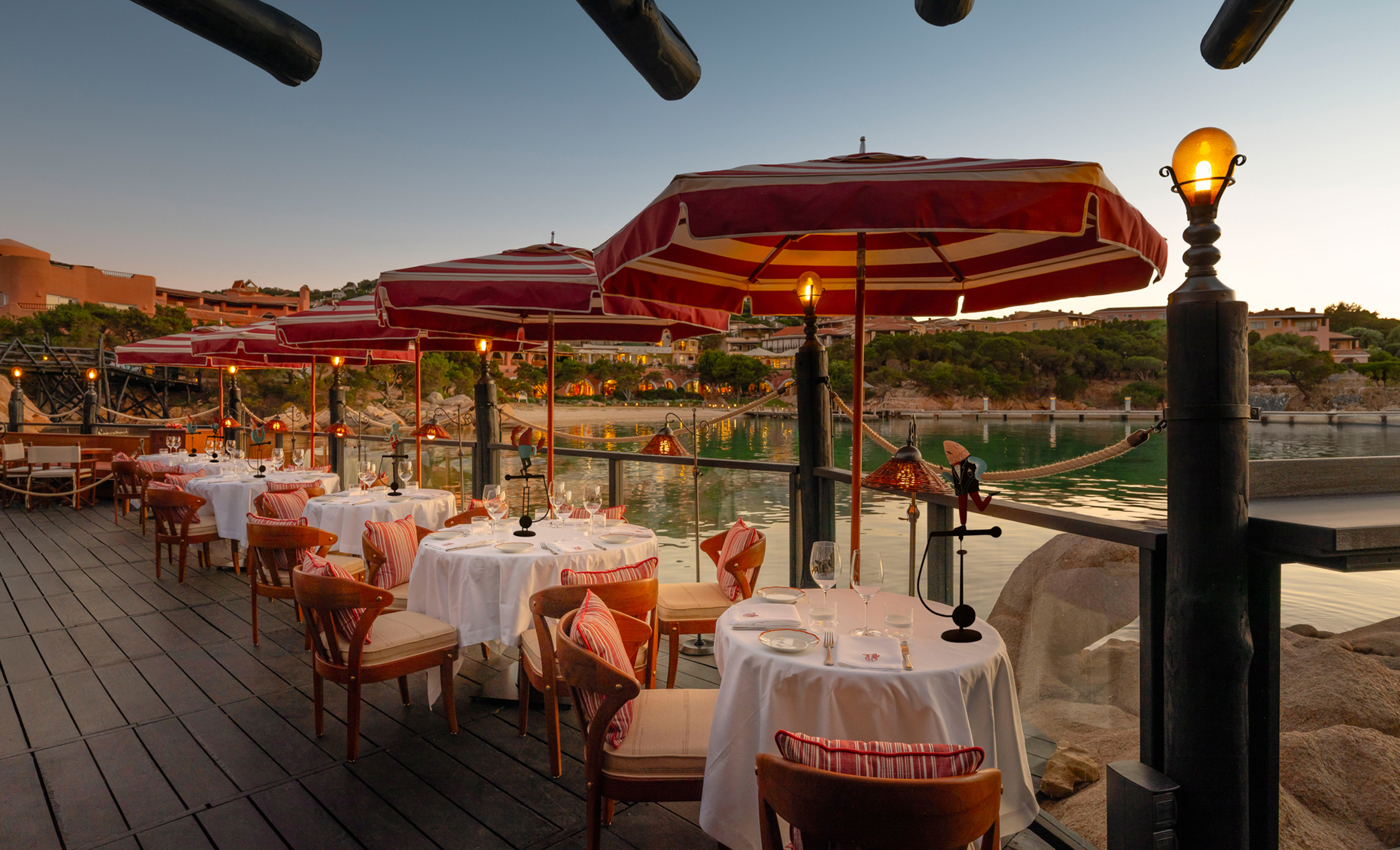Evening view of Langosteria Porto Cervo: Luce5 lighting solutions integrated across the reed ceiling, white plaster walls, and seafront cliff.