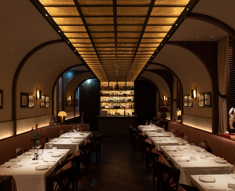 Evening view of Langosteria Porto Cervo: Luce5 lighting solutions integrated across the reed ceiling, white plaster walls, and seafront cliff. - column